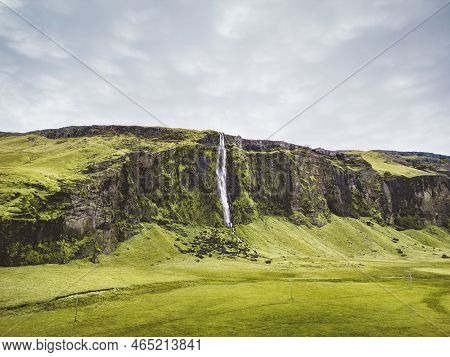 Drifandi Waterfall In Iceland, Grass Field And A Cliff With Waterfall Behind