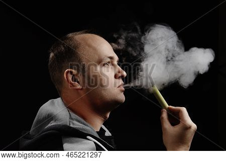 A Man Uses An Electronic Cigarette Against A Black Background. Space For Text. Alternative To Smokin