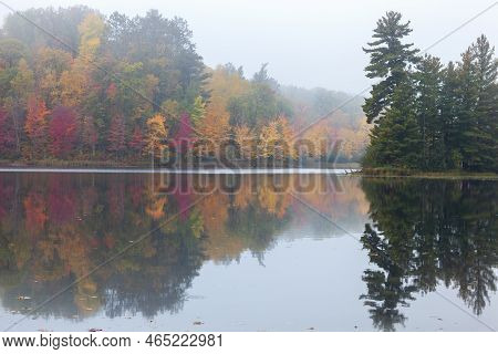 Foggy Trees In Autumn Color And A Small Island With Pines Reflect In The Water Of A Northern Minneso