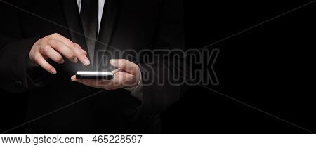 Business Person In Siut Hand Holding Smart Phone With Light Screen On Black Background
