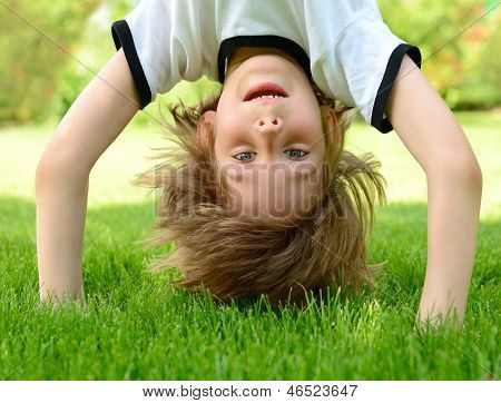 Glückliche kleine Junge stehend Kopf auf grünem Gras im Frühlingspark.