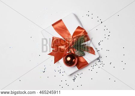 A Christmas Present Wrapped In Red Ribbon And Decorated With Pine Cones On A White Surface Surrounde