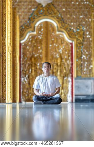 Asian Man Meditates On The Ground With Reflection In The Sunlight Pouring Into The Temple Church Wit