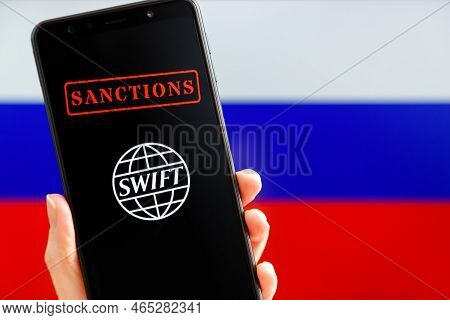 Ukraine, Kiev - February, 23 2022: Hand Holding Mobile With Swift Logo, Sanctions And Russian Flag I