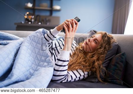 Woman Scrolling Smartphone, Web Surfing, Lying On Cozy Sofa At Stylish Living Room Under A Blanket. 