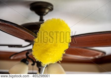 Using A Wand Feather Duster To Remove And Clean Dust From A Ceiling Fan