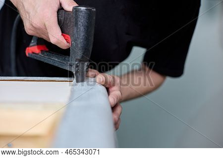 Production Of Upholstered Cabinet Furniture. Worker Qualitatively Fixes The Fabric With A Pneumatic 