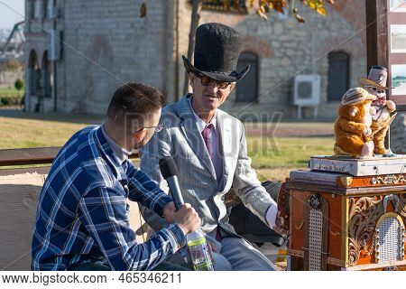 Bendery, Moldova - November 12, 2022: Organ Grinder In A Hat And Round Glasses Gives An Interview On