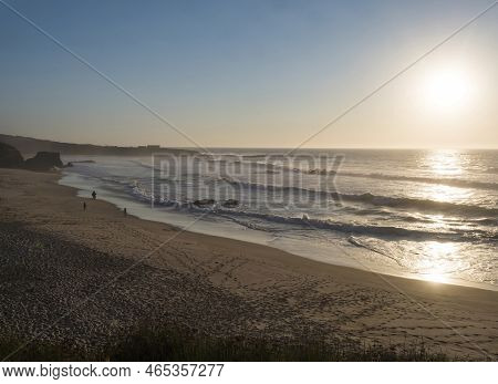 Praia Grande De Almograve Sand Beach With Distant Silhoutte Of People And Ocean Waves In Golden Hour