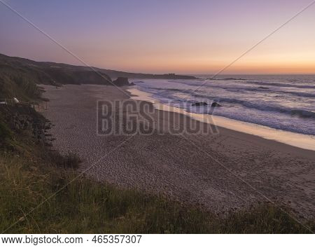 Sunset View Of Sand Beach Praia Grande De Almograve With Ocean Waves In Pink And Red Blue Hour Light