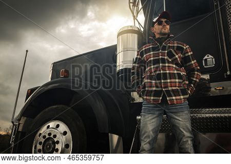 Caucasian Commercial Semi Truck Driver In His 40s In Front Of A Vehicle. Ground Transportation Theme