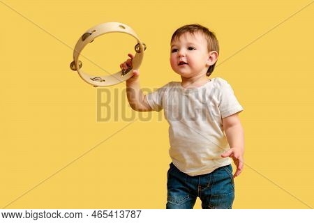 Toddler Baby Plays The Tambourine, A Child With A Percussion Musical Instrument On A Studio Yellow B