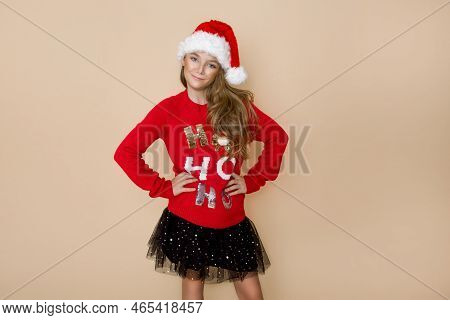Beautiful, Cute Little Girl, Wearing A Red Christmas Sweater And A Red Cap Of A Santa Claus.