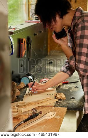 Cheerful Carpenter Woman Discussing Order Details With Her Customer On Smartphone