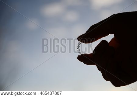 Caucasian Hand Compressing A Metal Spring Between A Thumb And Finger