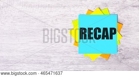 On A Light Gray Wooden Background, Bright Stickers With The Text Recap Annual General Meeting.