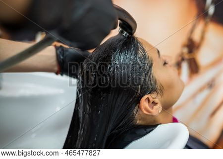 Female Client Washes Hair In Salon, Professional Hairdresser Washes Head Of Female Client With Water
