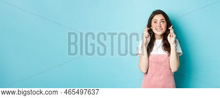 Portrait Of Hopeful Brunette Girl Cross Fingers For Good Luck, Making Wish, Looking Up With Begging 