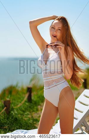 A Long-haired, Slender, Beautiful Woman In A Swimsuit By A Chaise Longue By Sea.