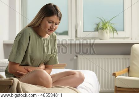 Young Woman Suffering From Menstrual Pain On Bed At Home, Space For Text