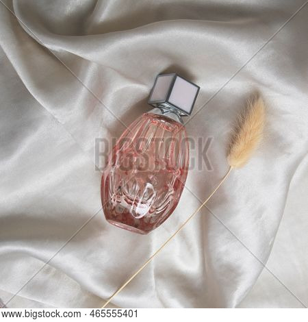 A Bottle Of Perfume In Pink Glass On A Background Of Silk Fabric. Minimalistic Fashion Photography