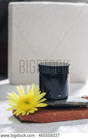 Black Cream Jar And Yellow Flower On Natural Stone Background. Skincare, Spa And Wellness Concept. C