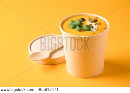Creamy Pumpkin Fall Soup In Craft Paper Food Container With Bamboo Spoon Against Orange Background W