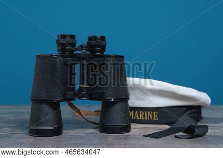 Old Marine Binoculars And Peakless Cap On A Turquoise Background On A Textured Wooden Table