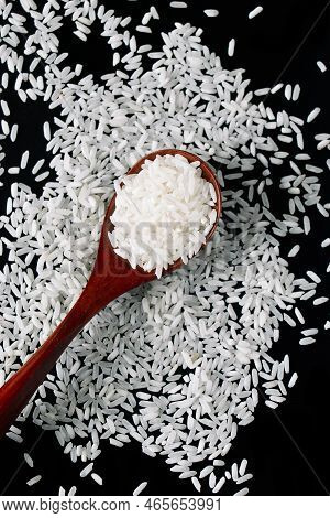 White Raw Rice In Wooden Spoons On Black Background. Natural Organic Vegan Food. Uncooked Grains Of 