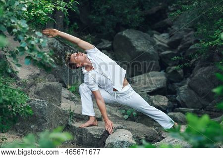 A Young Guy Does Yoga In Nature Among The Stones. Utthita Parshvakonasana - The Pose Of The Extended