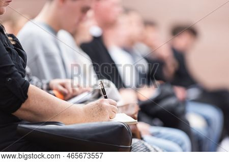 Female Hands Holding Pen And Notebook, Making Notes At Conference Lecture. Event Participants In Con