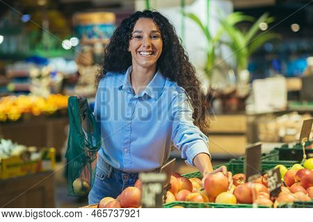 Portrait Of Happy Woman Shopper In Supermarket, Hispanic Woman Chooses Apples And Fruits Smiling And