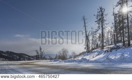 The Road Bends In A Snowy Valley. Snowdrifts On The Side Of The Road. Bare Trees On A Hill, Against 