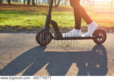 Young Woman Discover City And Park At Sunset With Electric Scooter Or E-scooter. Female Legs In Spor