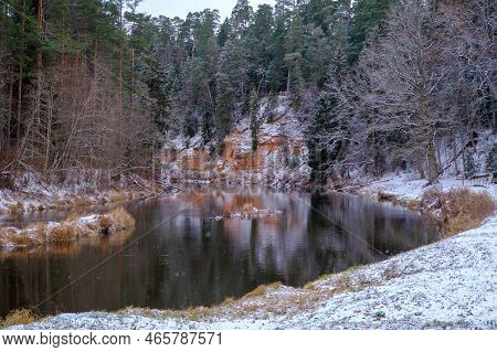 View Of Red Sandstone Cliffs. Salaca River. Skanaiskalns Nature Park. November Is The First Snow In 