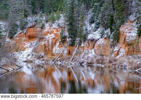 View Of Red Sandstone Cliffs. Salaca River. Skanaiskalns Nature Park. November Is The First Snow In 
