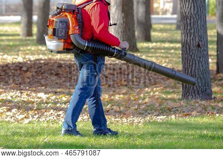Working In The Park Removes Leaves With A Blower. Park Cleaning Service. Removing Fallen Leaves In A