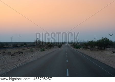 Pre Dawn Light In Desert Sky With Empty Road Passing Through The Desert. Wind Mills In The Horizon, 