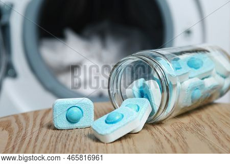 Jar With Water Softener Tablets On Wooden Table Near Washing Machine, Closeup