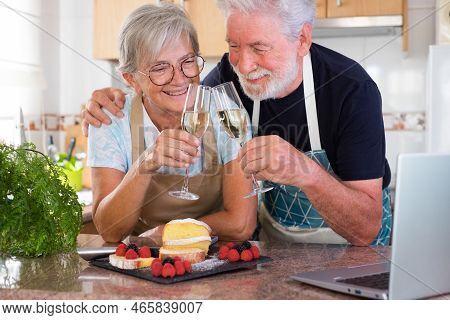 Cheerful Senior Couple In The Home Kitchen Toasting With Glasses Of Wine Ready To Eat Their Homemade