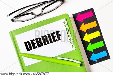 On A Light Background, Multi-colored Arrows, Black Glasses, A Green Notebook With A Pen And A White 