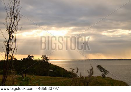 On The Coast Of Hundested. Sun Rays Break Through The Dramatic Sky Through The Clouds. Meadow In The