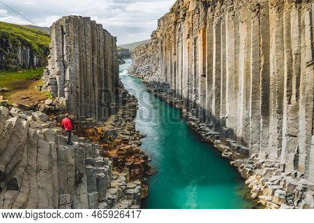 Man Hiker In Red Jacket Visit Studlagil Basalt Canyon, With Rare Volcanic Basalt Column Formations, 
