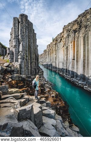 Woman Hiker With Backpack Visit Epic Studlagil Canyon. Unique Jokulsa Basalt Colums And A Bru River.