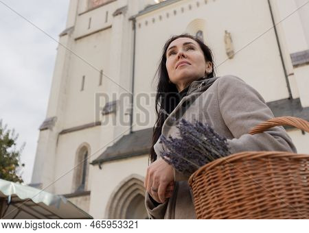 A Woman Stands With A Shopping Basket In Her Hands Against The Backdrop Of A Tall Light Building, Au