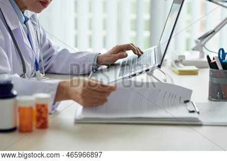 General Practitoner Checking Medical Documents And Working On Laptop
