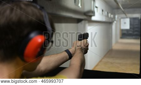 Close-up Of Man In Tactical Headphones Aiming Gun At Target In Shooting Range. Shooting Practicing W