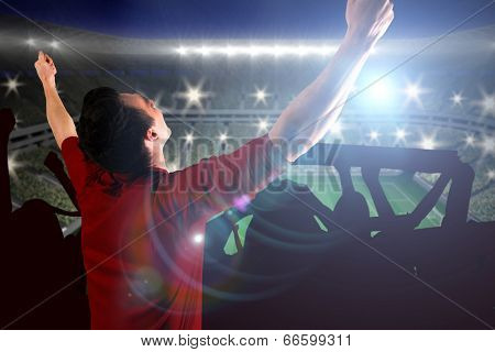 Cheering football fan in red jersey against large football stadium with lights