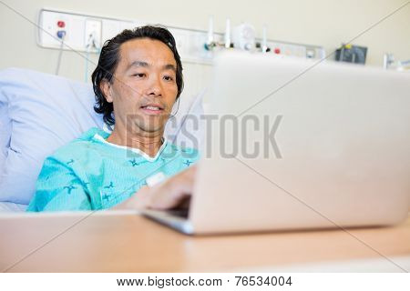 Mature male patient using laptop on bed in hospital