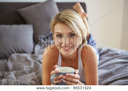 Happy smiling beautiful blond woman awaking with cup of coffee